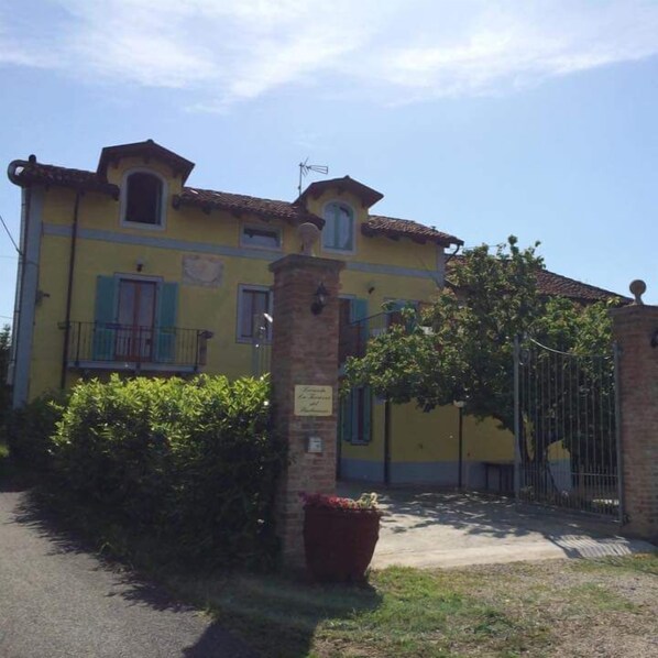 A yellow building with a balcony, a gate, and a potted plant. - La Terrazza del Barbaresco (Neviglie)