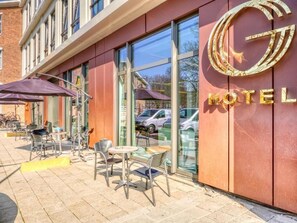 A hotel exterior with a prominent logo, outdoor seating area, and a clear view of parked cars through the windows. - Camp Inn Hotel Amsterdam (Amsterdam)