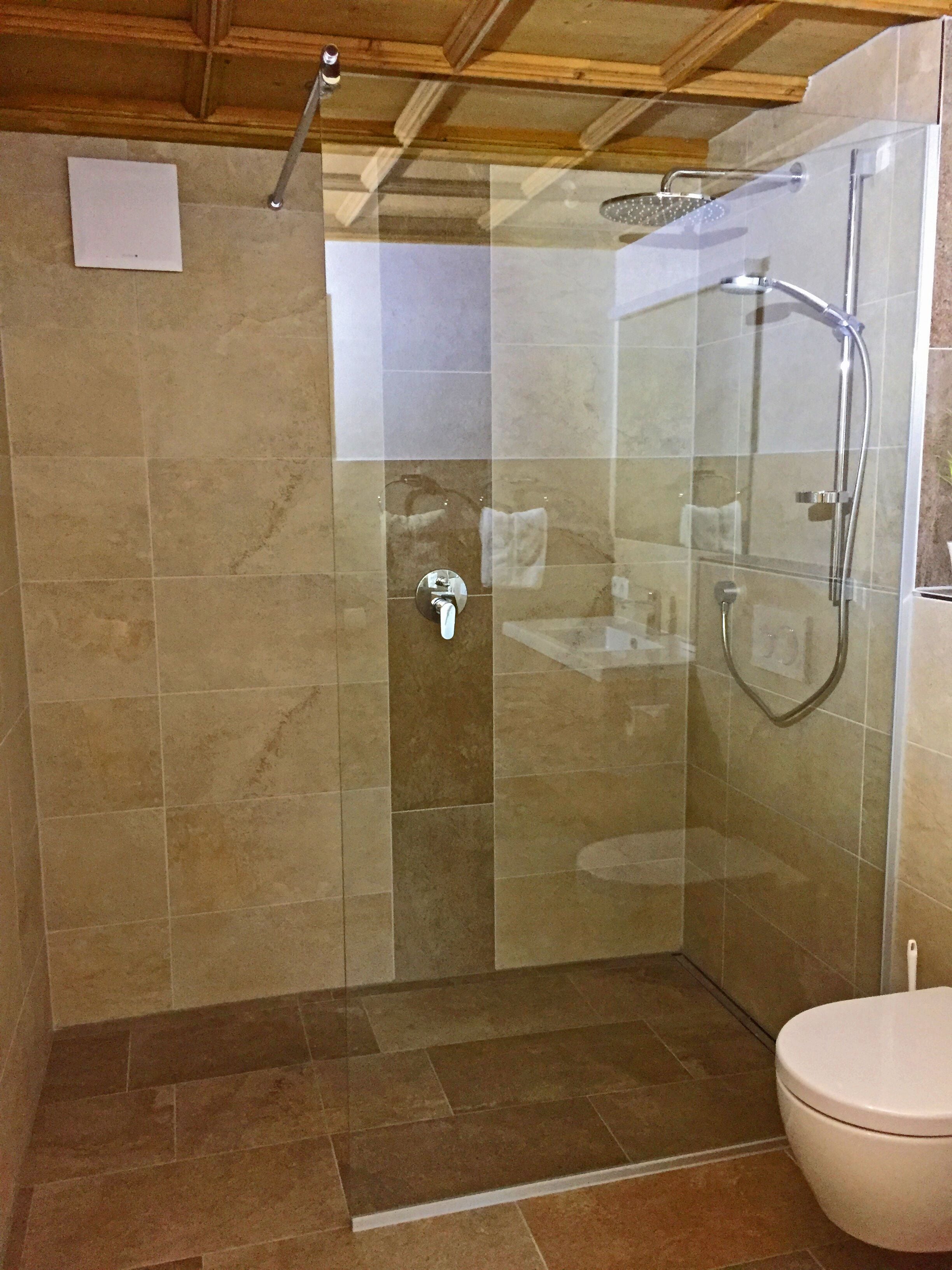 A glass-enclosed shower with a handheld showerhead and a wall-mounted faucet.