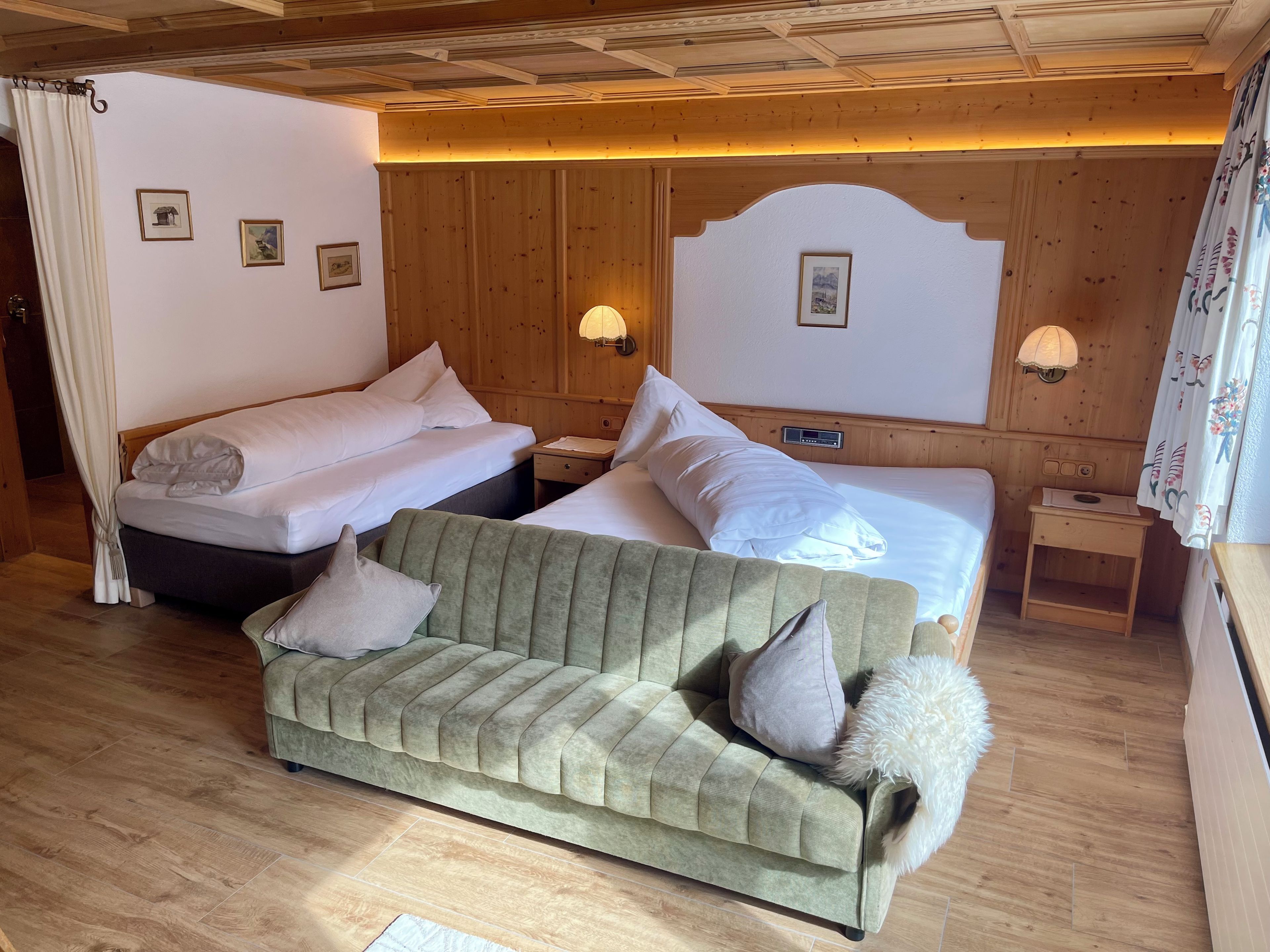 A hotel room with a bed, a sofa, a nightstand, and a wall-mounted lamp.