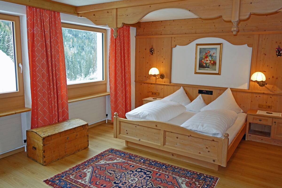 A wooden bedroom with a bed, nightstands, a wooden chest, and a window with curtains.