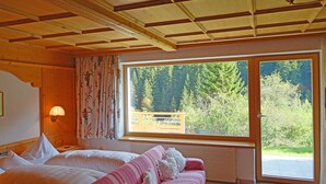 A room with a bed, a sofa, and a large window with a view of trees. - Alkira (Sankt Anton am Arlberg)