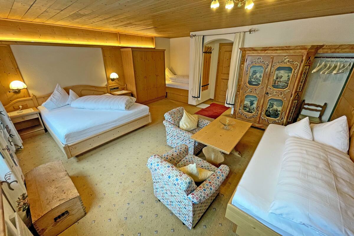 A cozy hotel room with a large bed, a smaller bed, a sofa, a table, and a mirror.