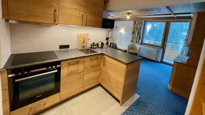 A modern kitchen with wooden cabinets, a built-in oven, and a large island with a sink. - Alkira (Sankt Anton am Arlberg)