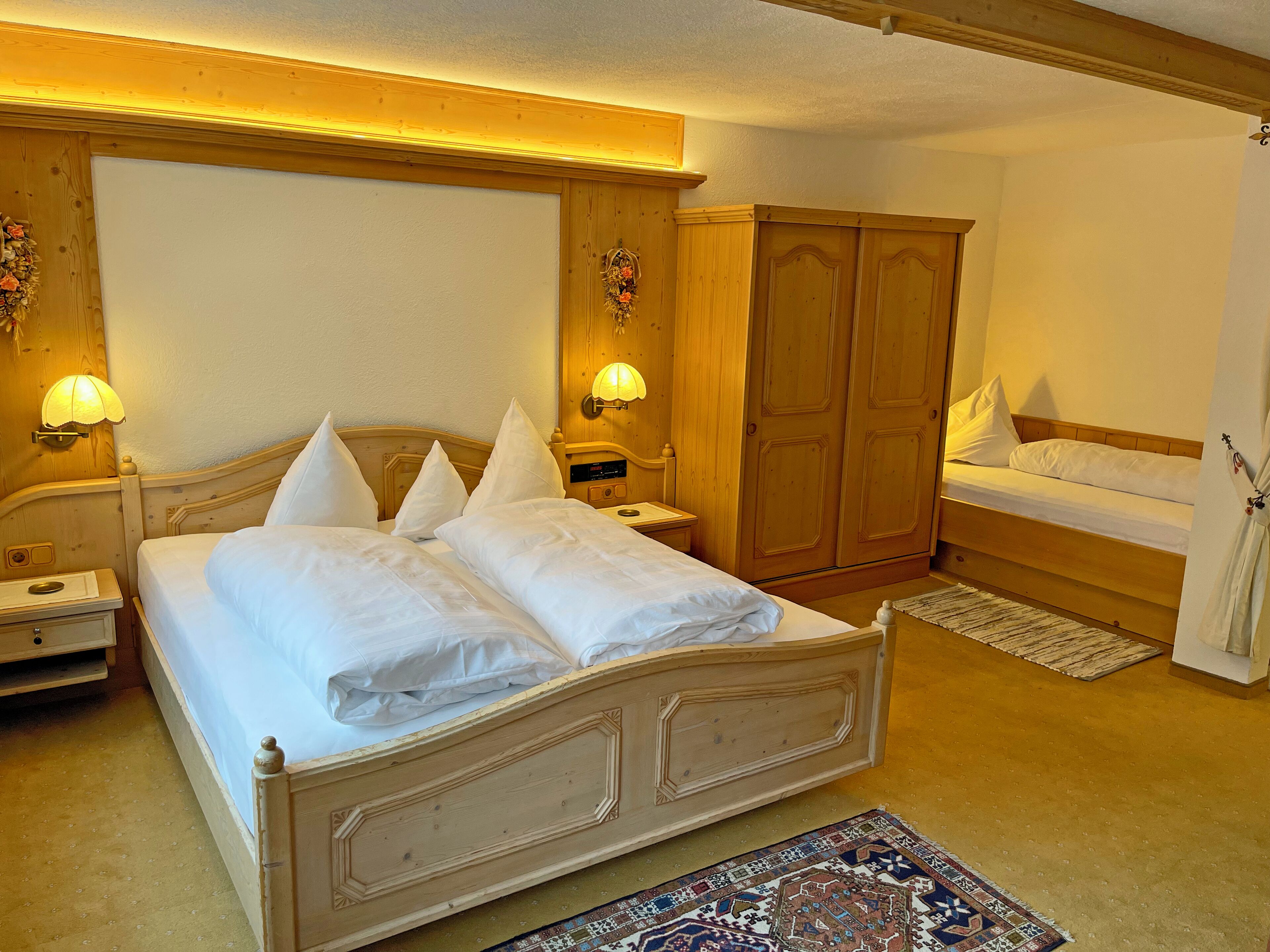 A bedroom with a large bed, a smaller bed, a wardrobe, and two bedside lamps.