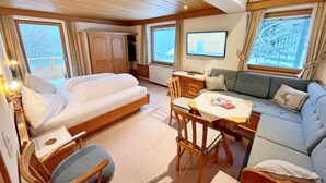 A cozy cabin room with a bed, sofa, dining table, and a TV. - Alkira (Sankt Anton am Arlberg)