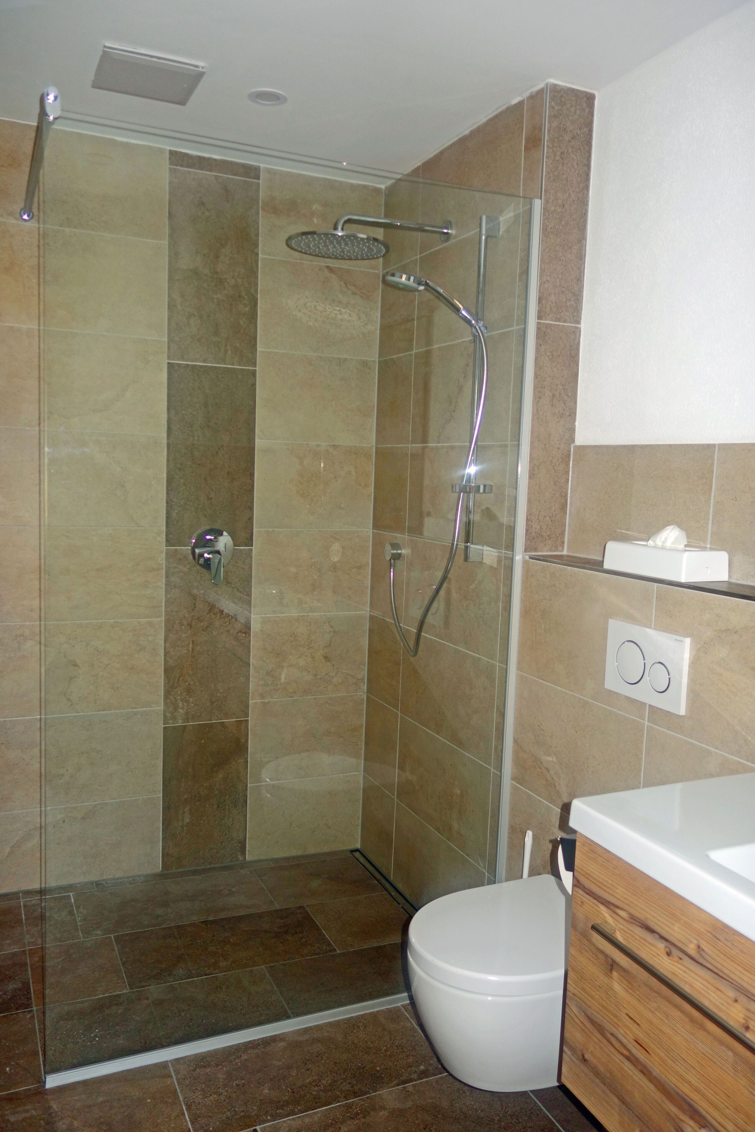 Een moderne badkamer met een glazen douchecabine, toilet en een houten wastafelmeubel.