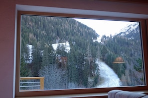 A room with a large window offering a view of a forested mountain area. - Alkira (Sankt Anton am Arlberg)