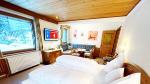 A hotel room with a large bed, a desk with a chair, a sofa, and a TV mounted on the wall. - Alkira (Sankt Anton am Arlberg)