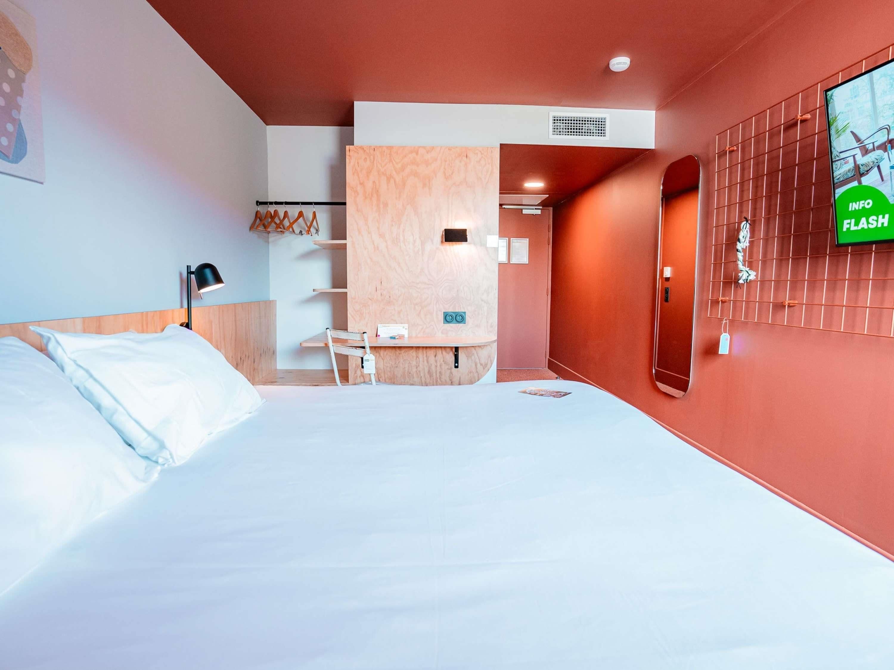 A modern hotel room with a bed, a desk, and a TV mounted on the wall.