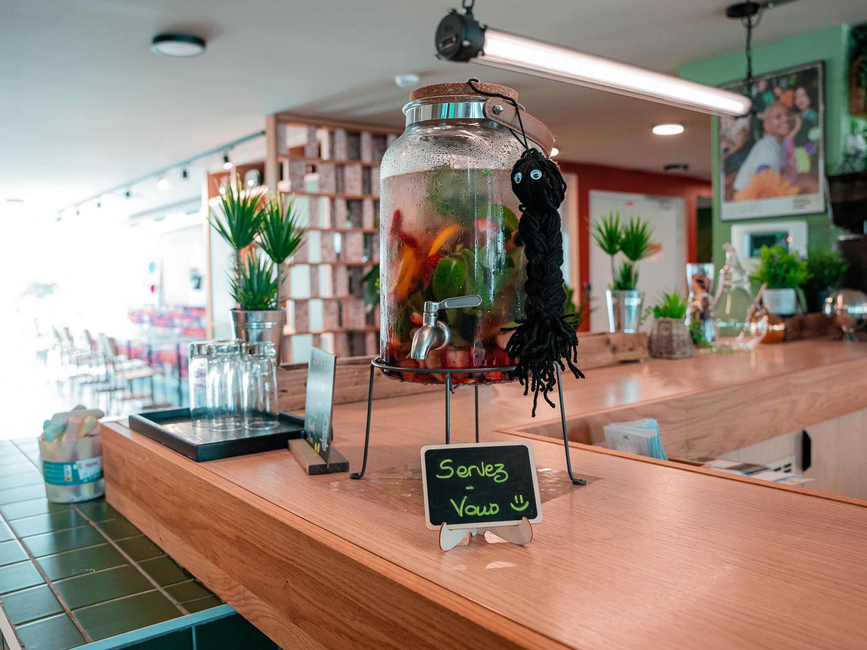 A bar area with a clear drink dispenser, a chalkboard sign, and potted plants.