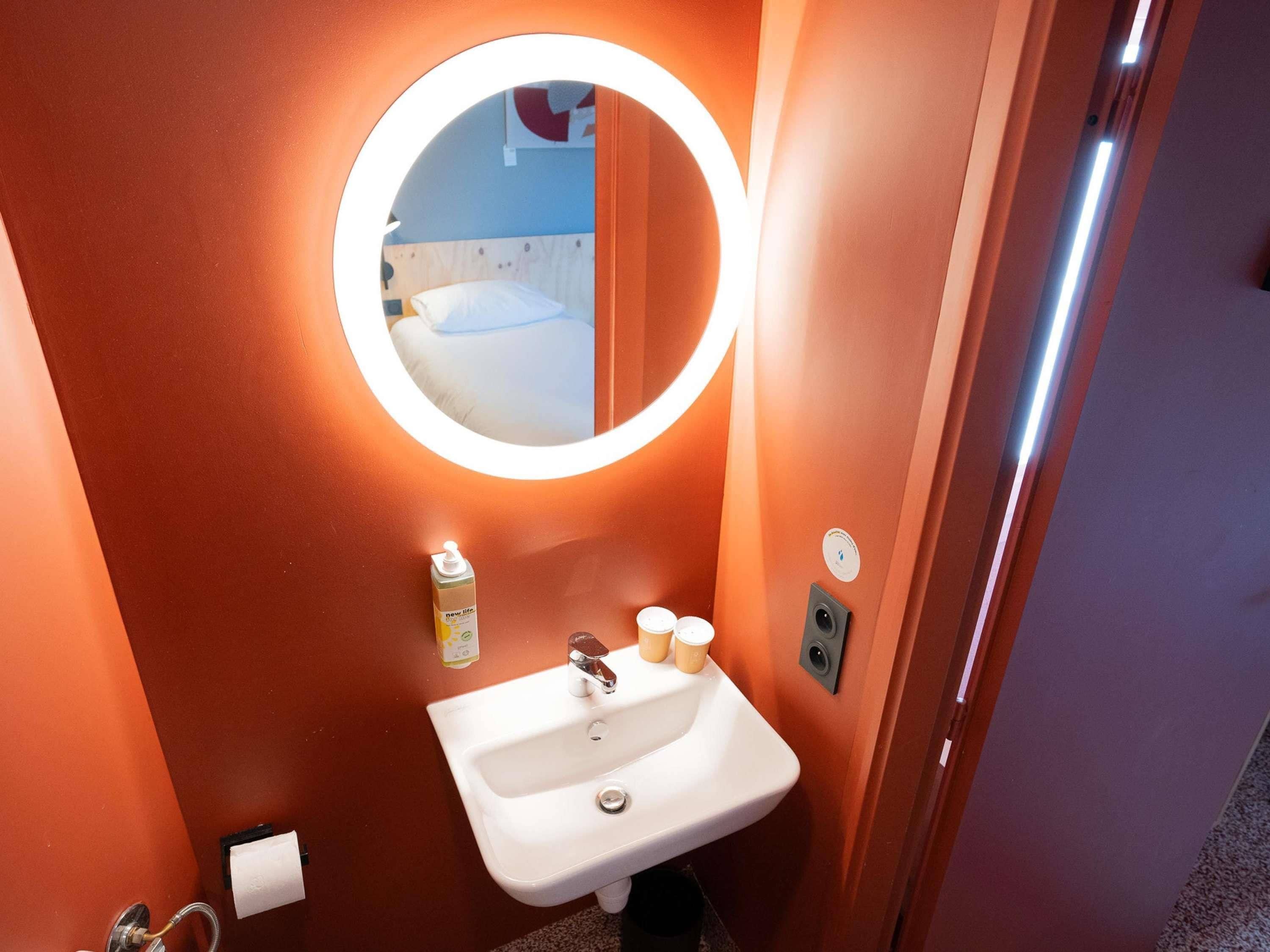 A bathroom with a round mirror, white sink, and a bottle of hand soap.