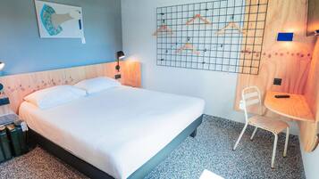 Quarto de hotel com cama, poltrona, escrivaninha, televisão na parede e uma obra de arte na parede.