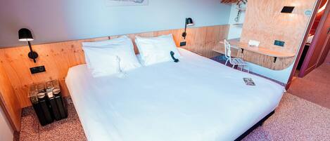 A hotel room with a large bed, wooden headboard, two bedside tables, a small desk, and a mirror.