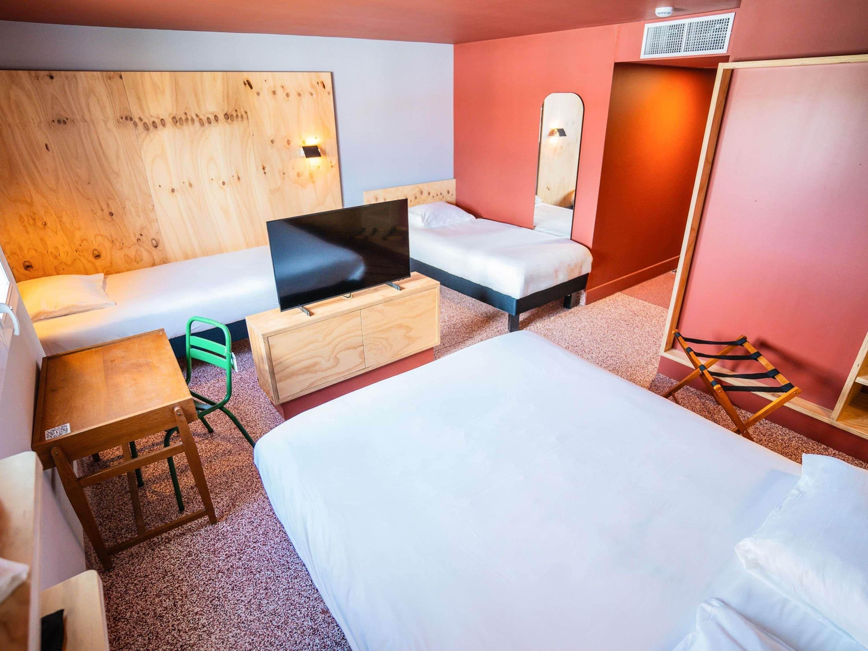 A hotel room with a bed, a sofa, a TV on a wooden cabinet, a small table, a chair, and a mirror.