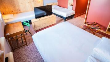 A hotel room with a bed, a sofa, a TV on a wooden cabinet, a small table, a chair, and a mirror.