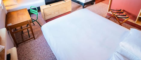 A hotel room with a bed, a sofa, a TV on a wooden cabinet, a small table, a chair, and a mirror.
