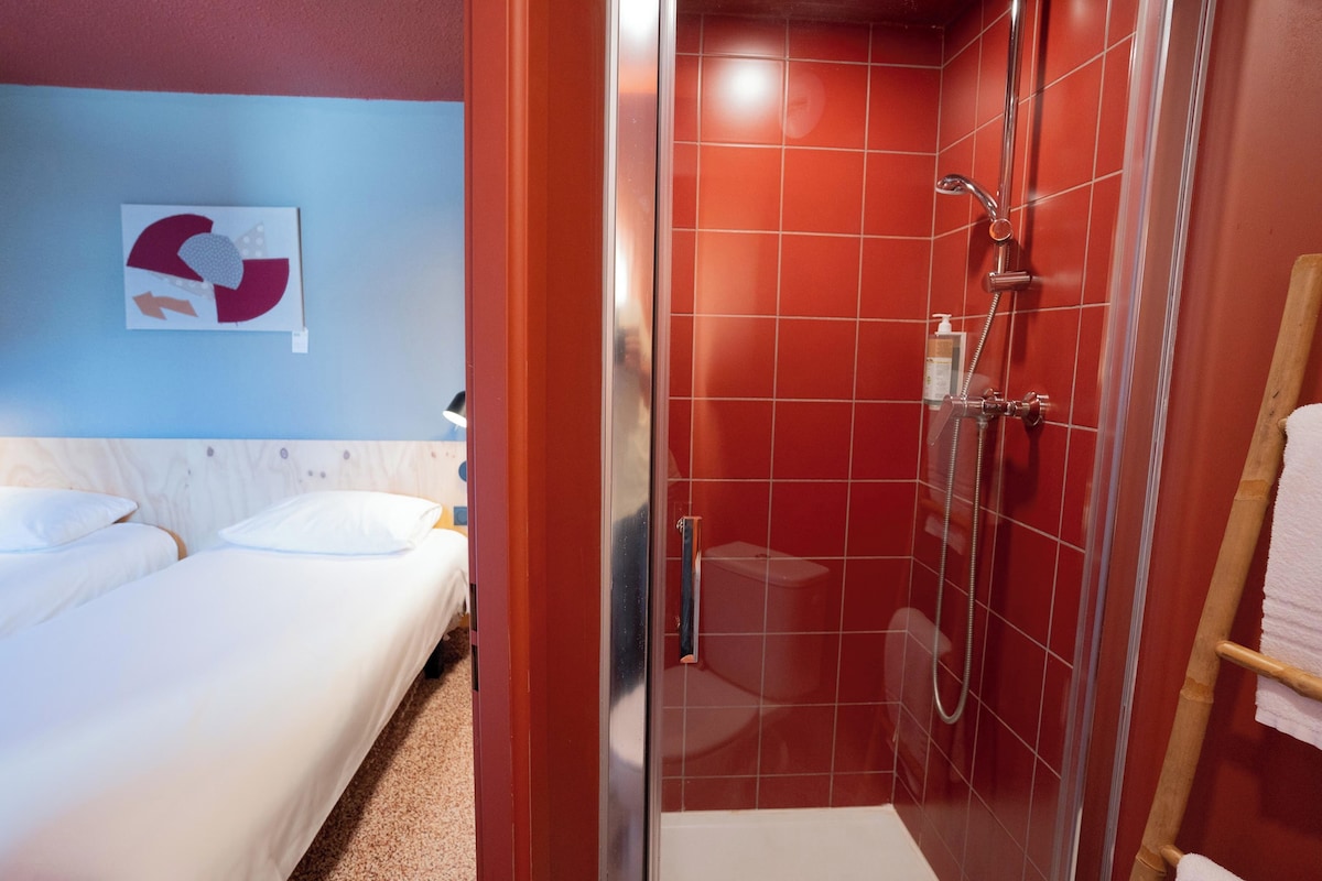 Una habitación de hotel con cama, ducha y pared de baldosas rojas.