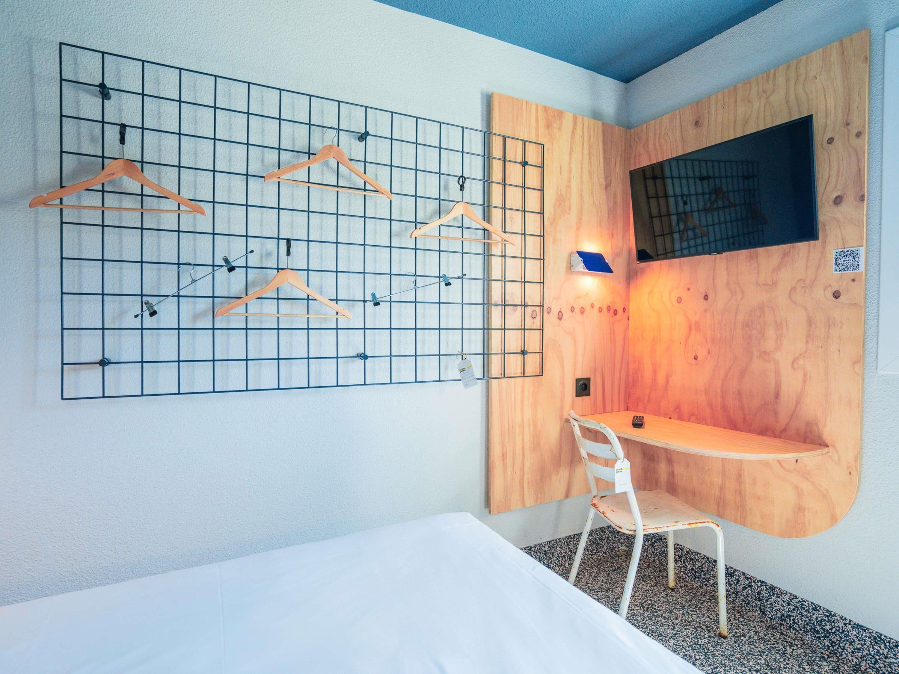 A compact room with a bed, a desk, a chair, and a wall-mounted grid with hangers.