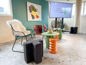 A modern interior with a green chair, a white furry chair, a colorful abstract painting, a television, and a unique table with stacked stools.
