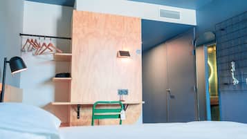 A modern hotel room with a bed, a desk with a chair, a wardrobe, and a mirror.