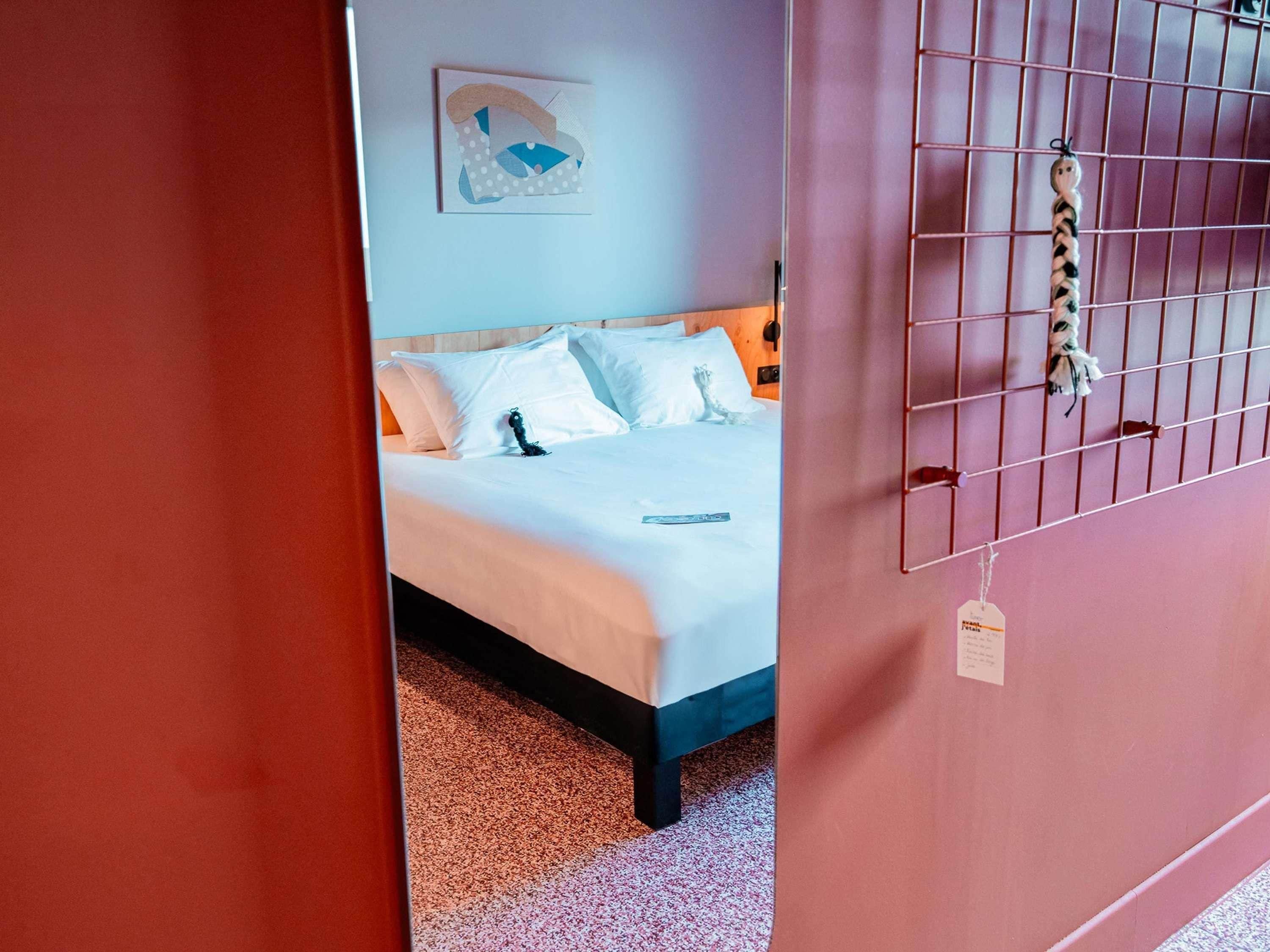 Un dormitorio con cama, almohadas blancas, cabecera azul, un perchero con una etiqueta y un cuadro sobre la cama.