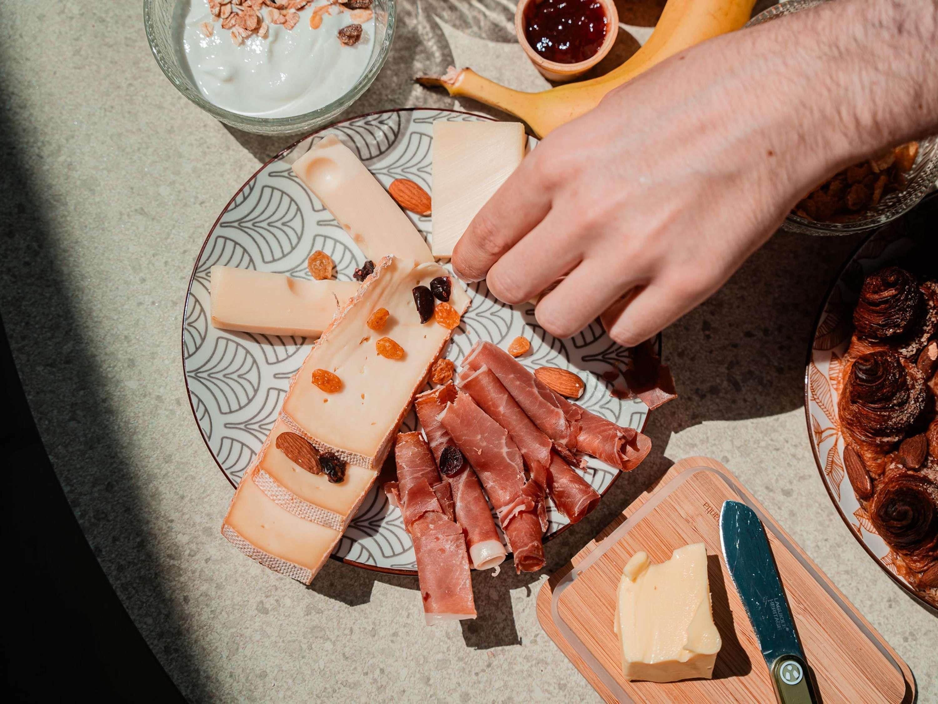 Eine Käseplatte mit verschiedenen Käsesorten, Prosciutto und Nüssen auf einem gemusterten Teller.