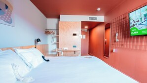 Una habitación de hotel con cama, escritorio, silla, televisor y pantalla montada en la pared.