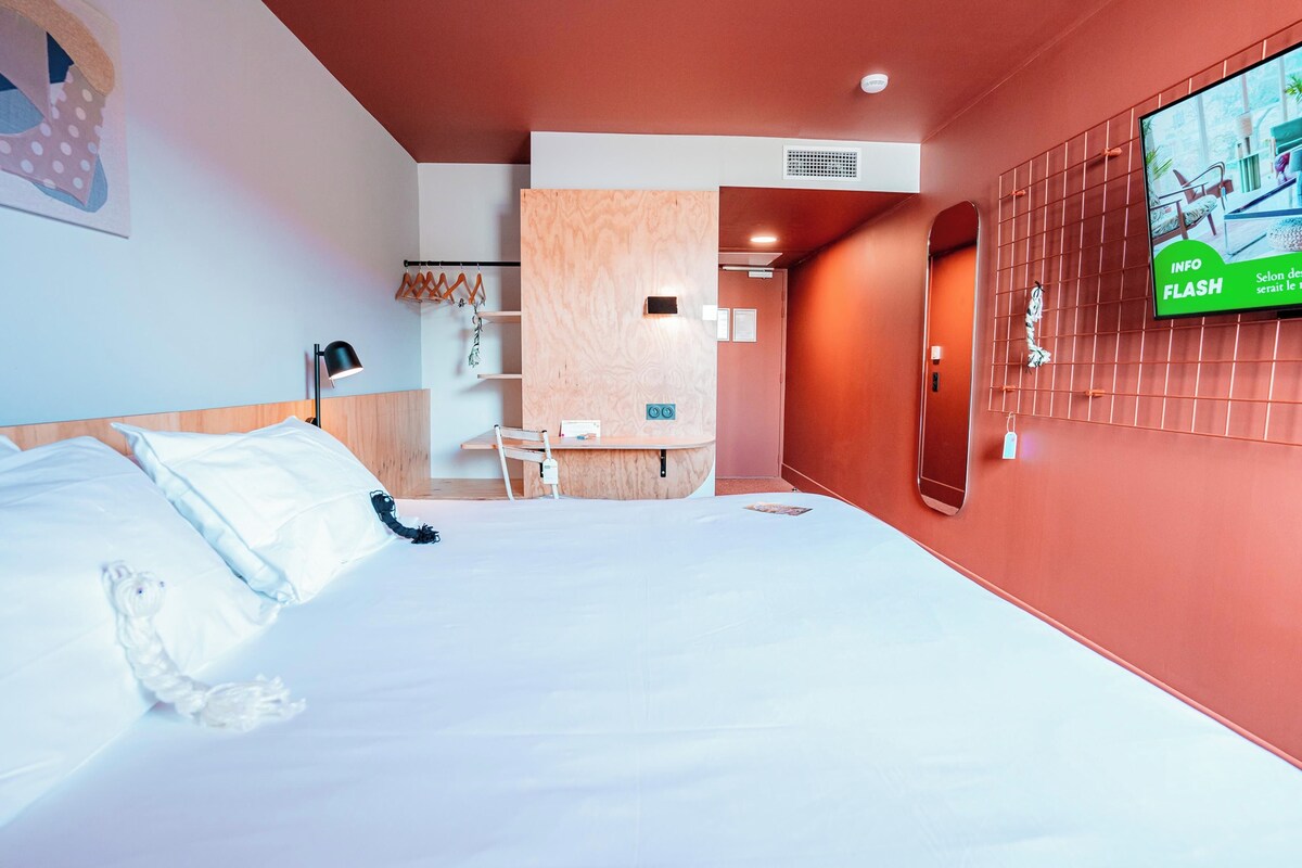 Una habitación de hotel con cama, escritorio, silla, televisor y pantalla montada en la pared.