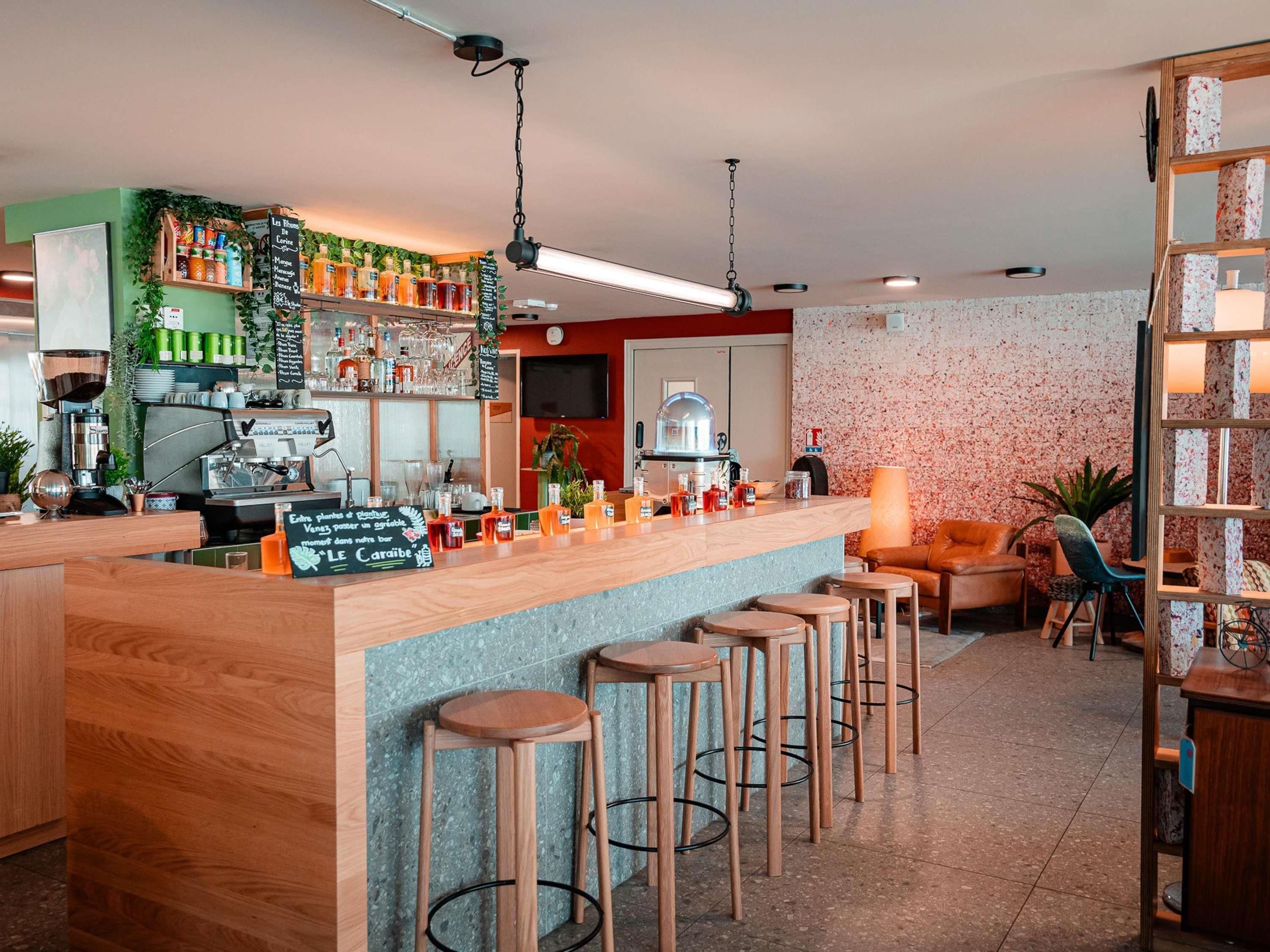 Zona de bar con taburetes, una máquina de café y estantes con botellas y vasos.