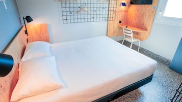 Ein Einzelbett mit Holz Kopfteil, ein Schreibtisch mit Stuhl und ein an der Wand befestigtes Gitter mit Holzaufhänger.