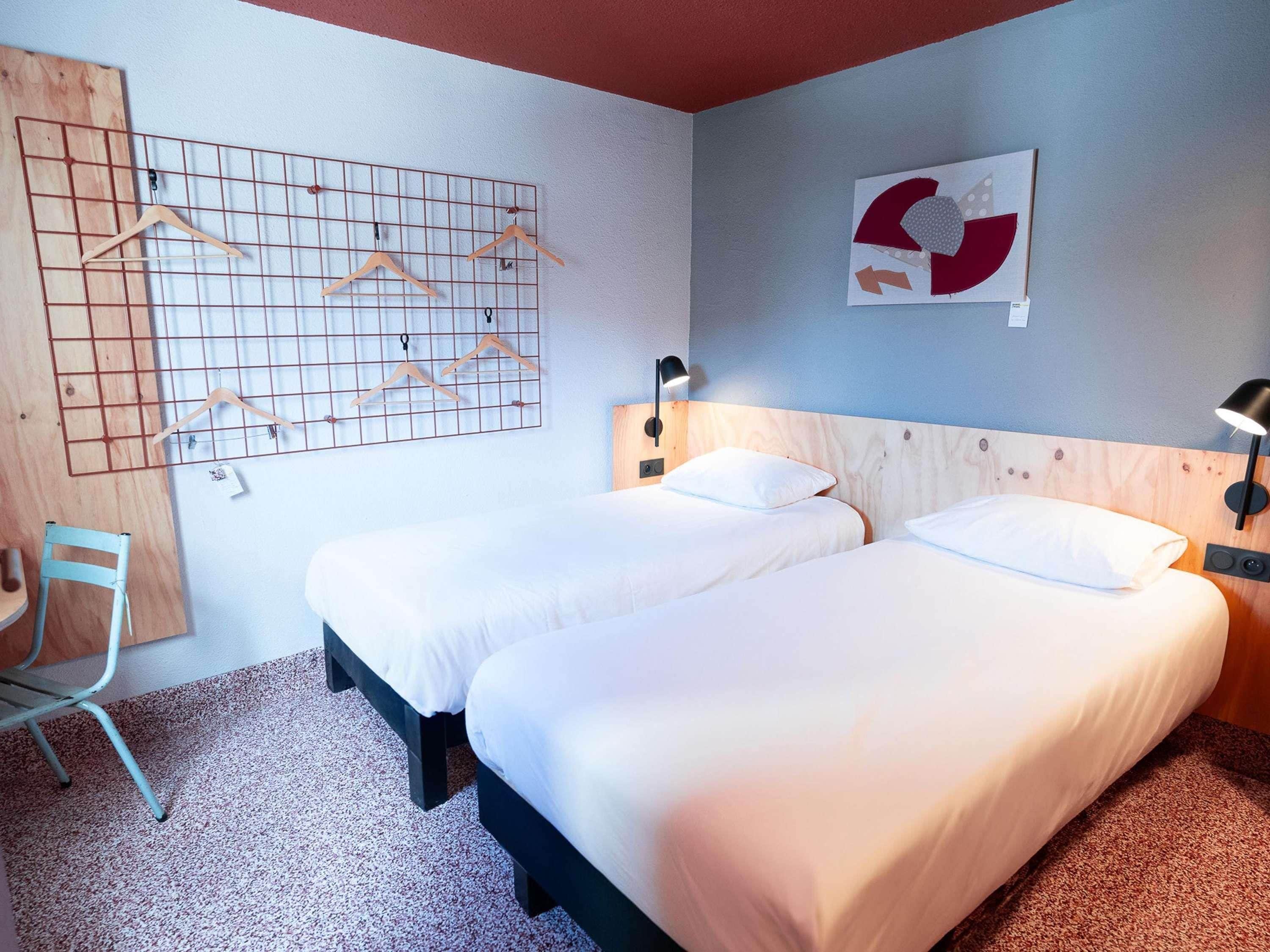 Habitación de hotel con dos camas, cabecero de madera, lámpara de pared y decoración en la pared con diseño de cuadrícula.