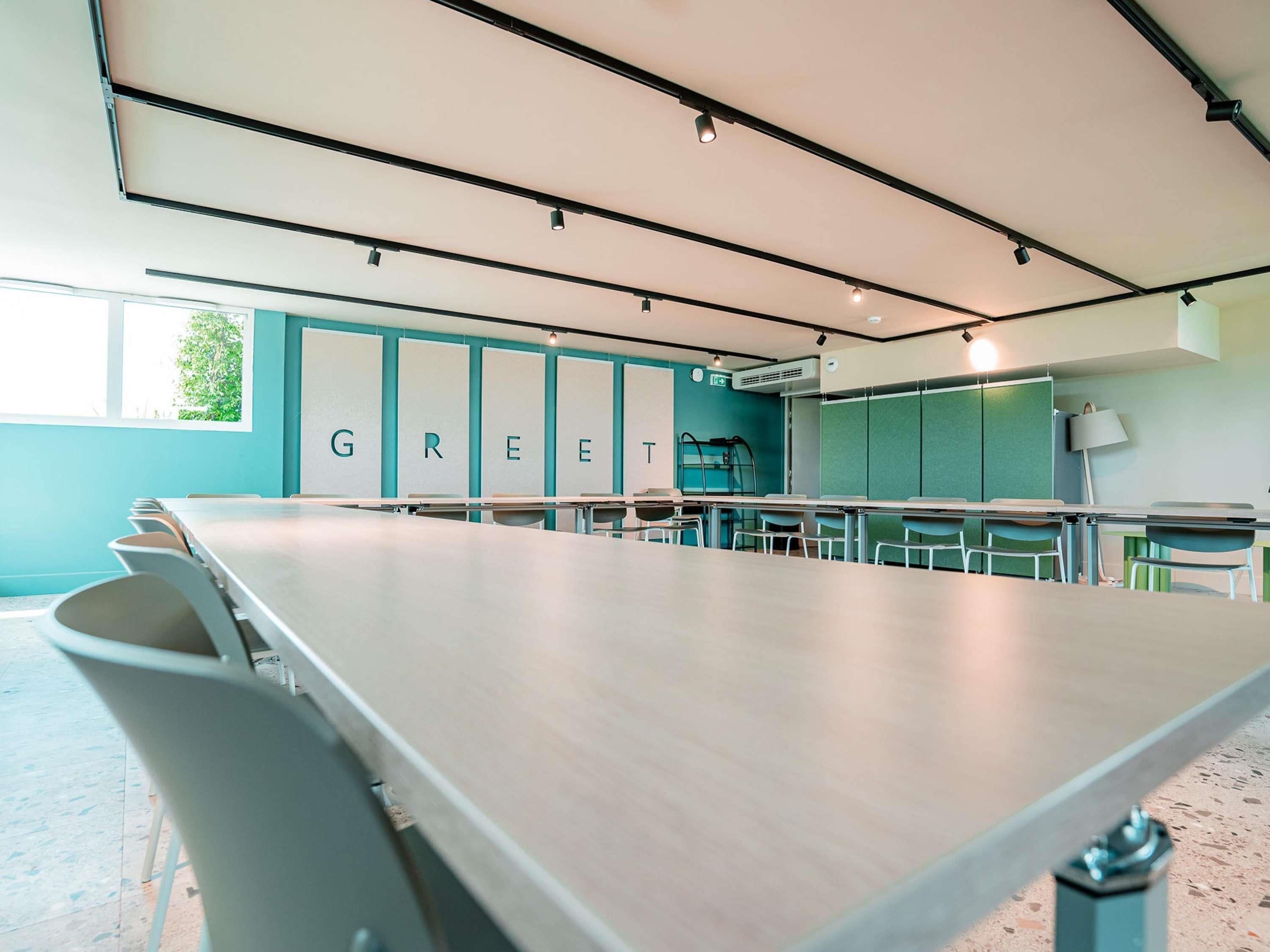 Une salle de conférence avec une longue table, des chaises et un mur sur lequel est inscrit le mot « VERT ».