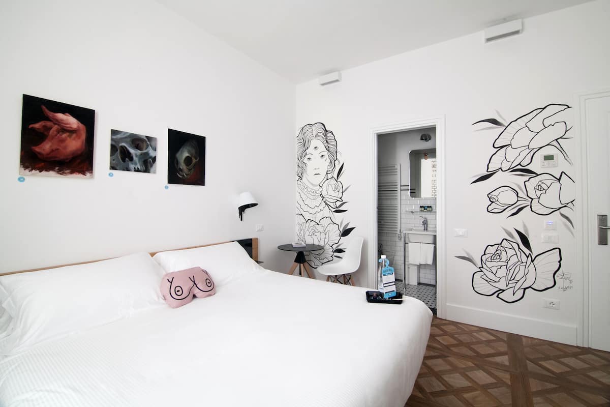 Habitación de hotel con cama, una mesita y una silla, y obras de arte en las paredes.