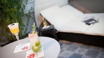 Una mesa con dos bebidas y una servilleta con un logotipo, una cama con un almohadón y una revista, y una planta al fondo.