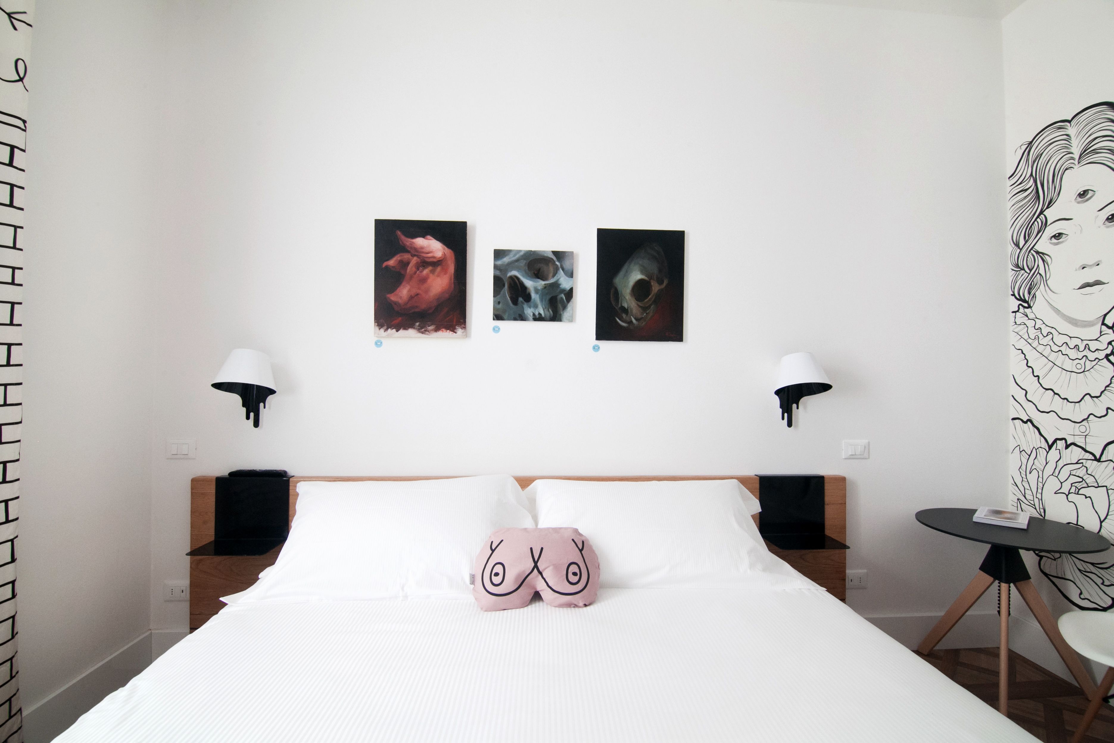 A hotel room with a bed, two bedside lamps, a small table, and three wall-mounted artworks.