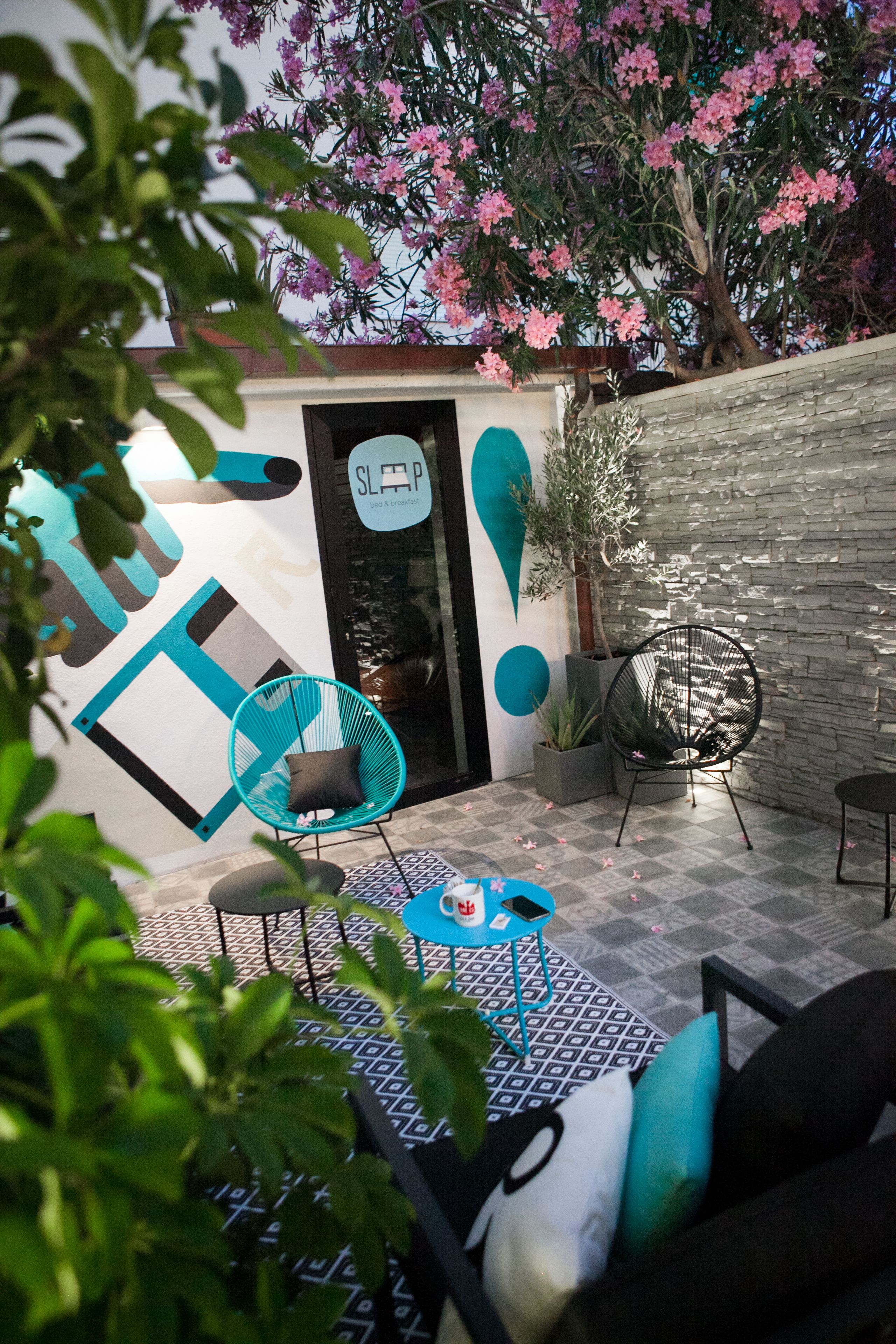 An outdoor seating area with a patterned floor, a blue chair, a small table, and a potted plant.