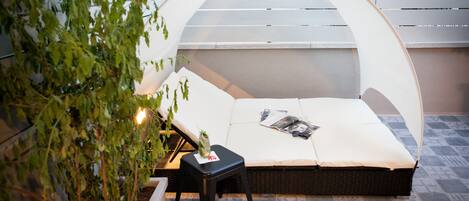 Un espace extérieur accueillant, aménagé avec un banc rembourré, une petite table et un pot de fleurs.