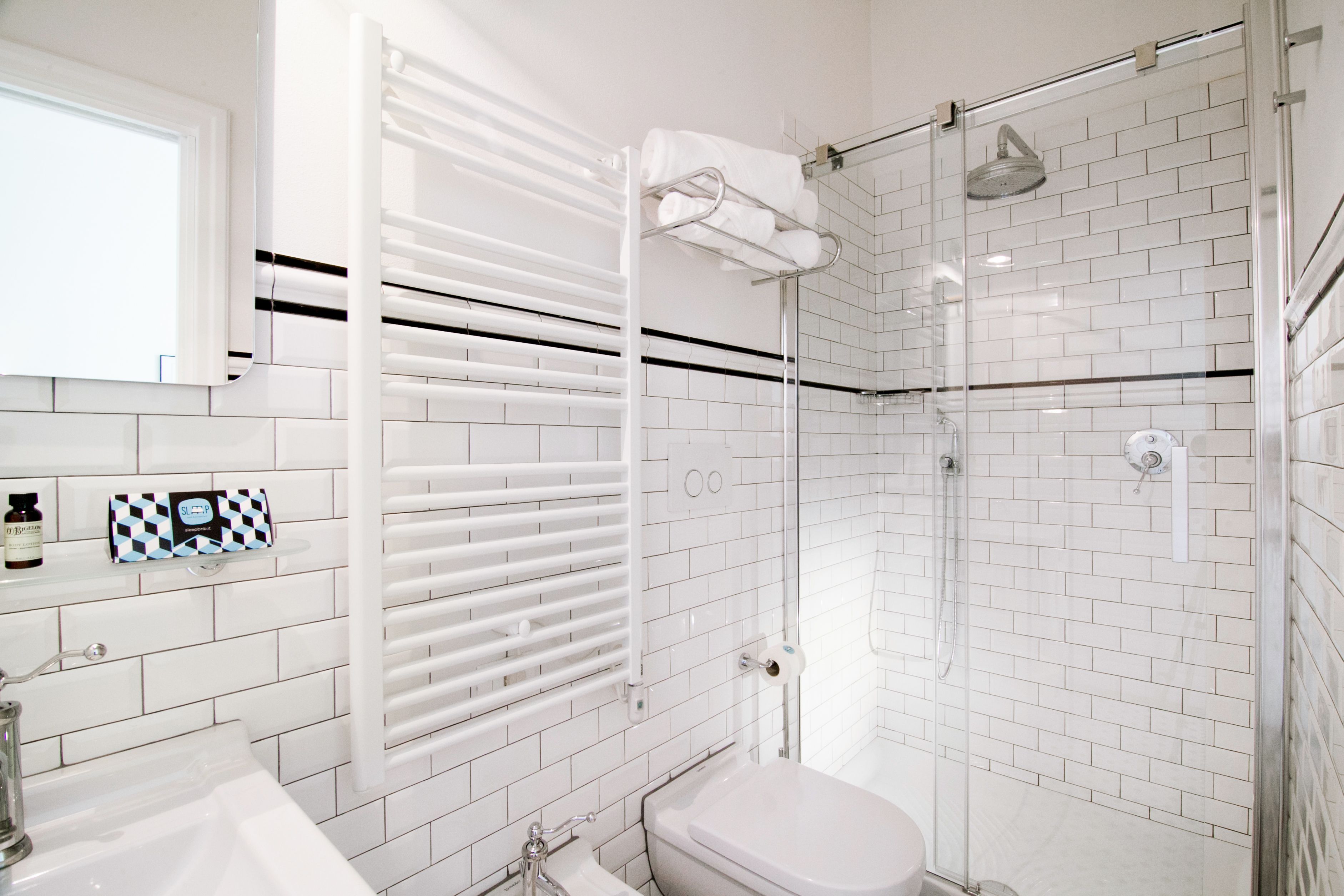 Un baño moderno con azulejos blancos tipo metro, cabina de ducha de vidrio, inodoro blanco y toallero con toallas dobladas.