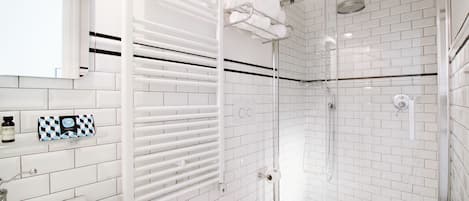 Un baño moderno con azulejos blancos tipo metro, cabina de ducha de vidrio, inodoro blanco y toallero con toallas dobladas.