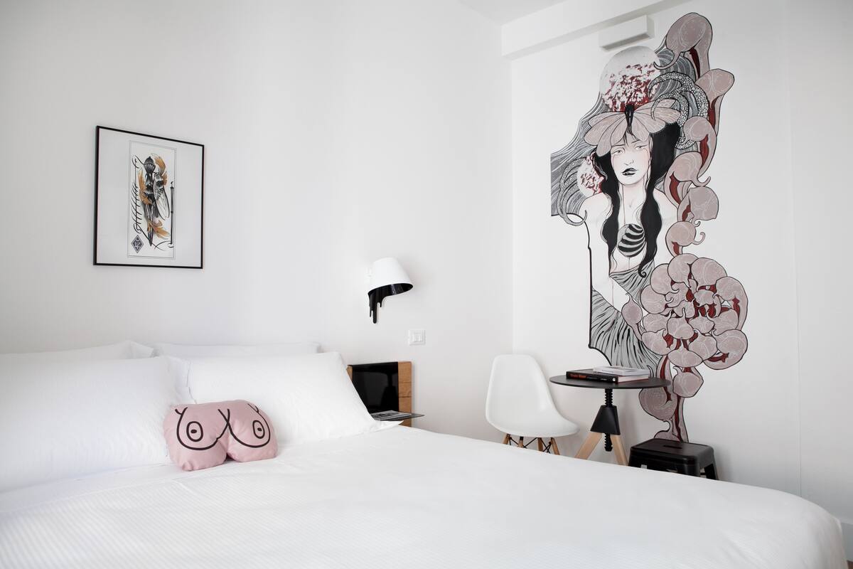 Una habitación de hotel moderna con una cama grande, un escritorio, una silla y una obra de arte en la pared.