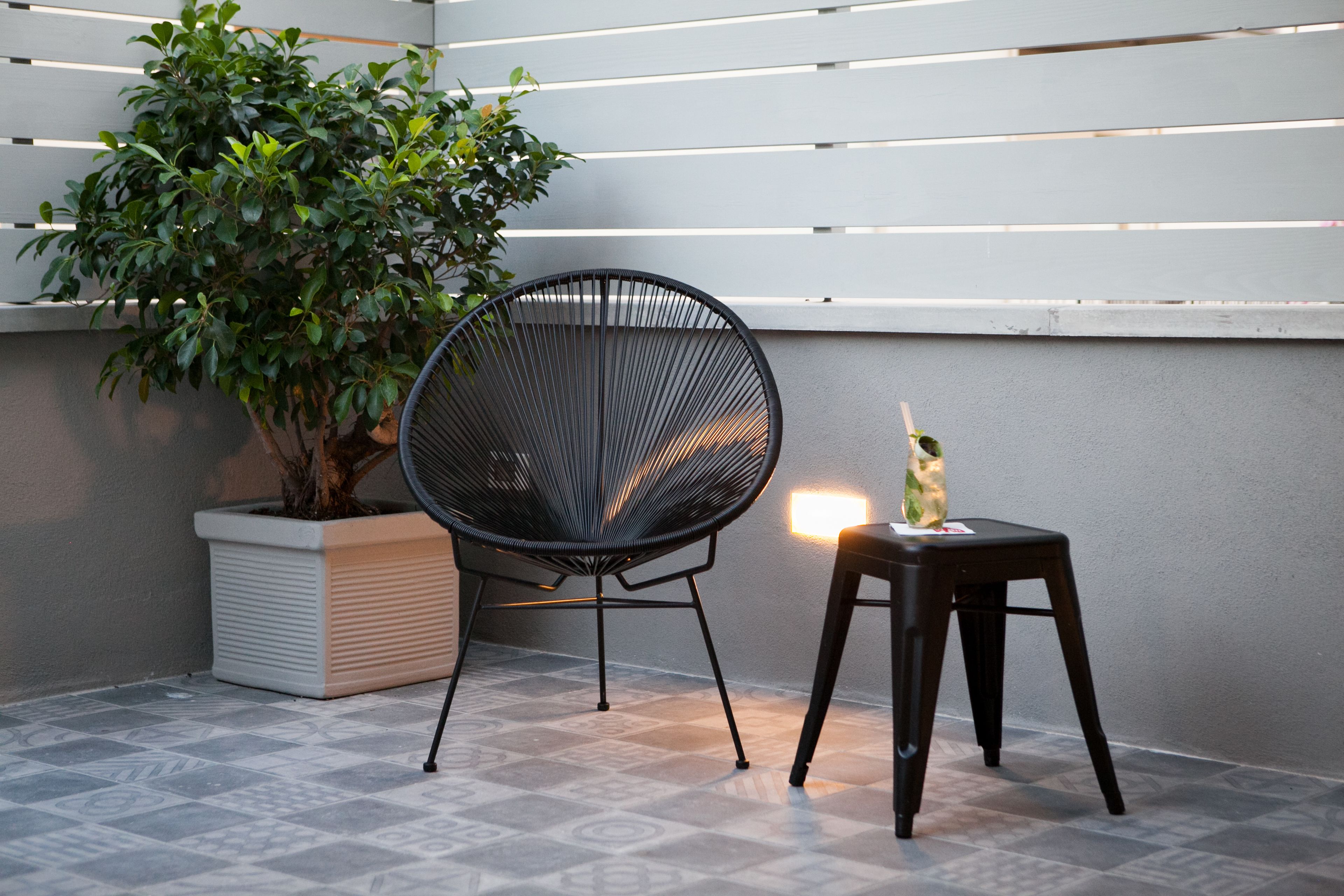 A corner with a potted plant, a black chair, and a small stool.