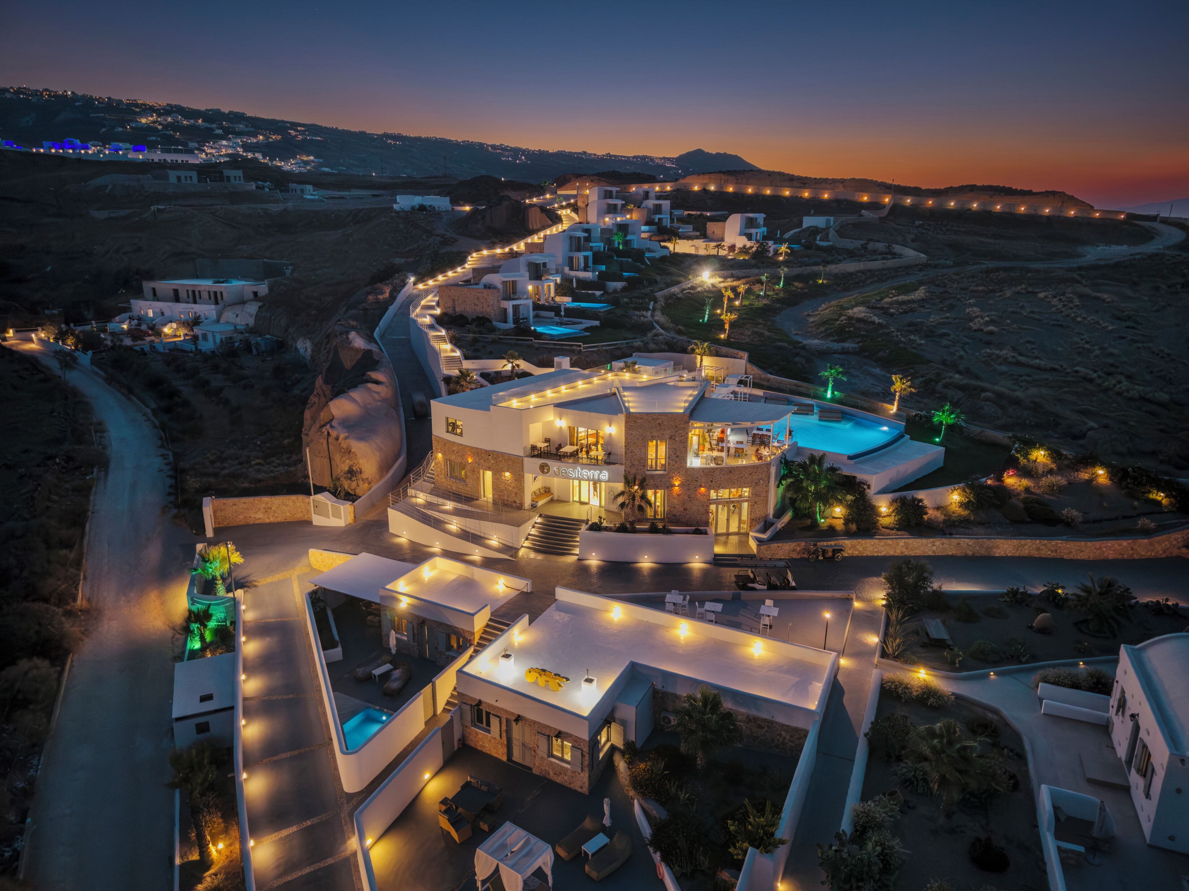A modern resort with a pool, multiple guest rooms, and a well-lit landscape.