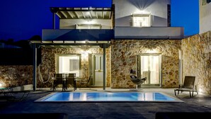 Un edificio moderno de dos pisos con fachada de piedra, piscina exterior y zona de estar al aire libre.