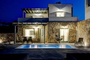 Un bâtiment moderne à deux étages, doté d’une façade en pierre, d’une piscine extérieure et d’un espace de détente en plein air.