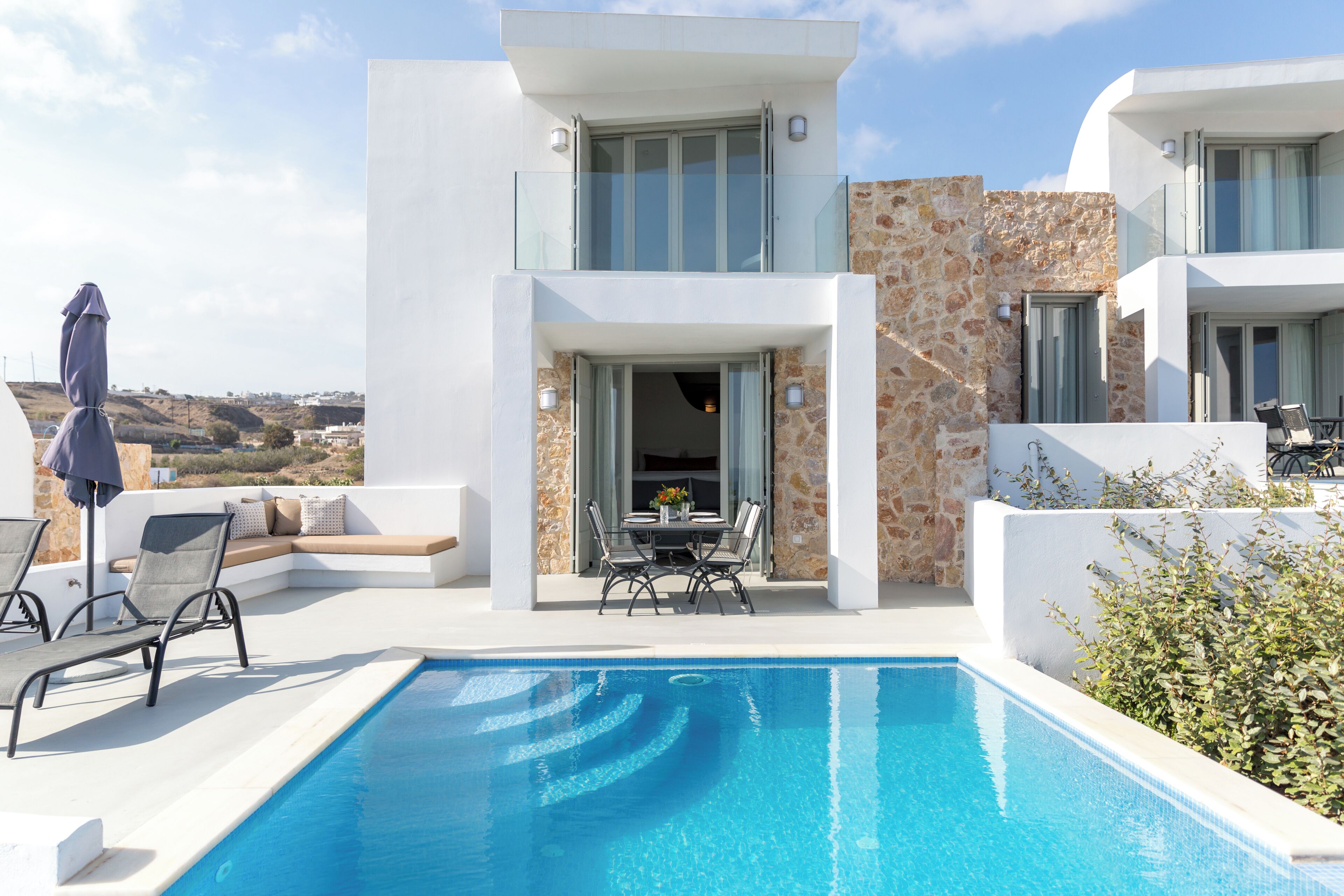 A modern villa with a pool, outdoor seating, and a view of the landscape.