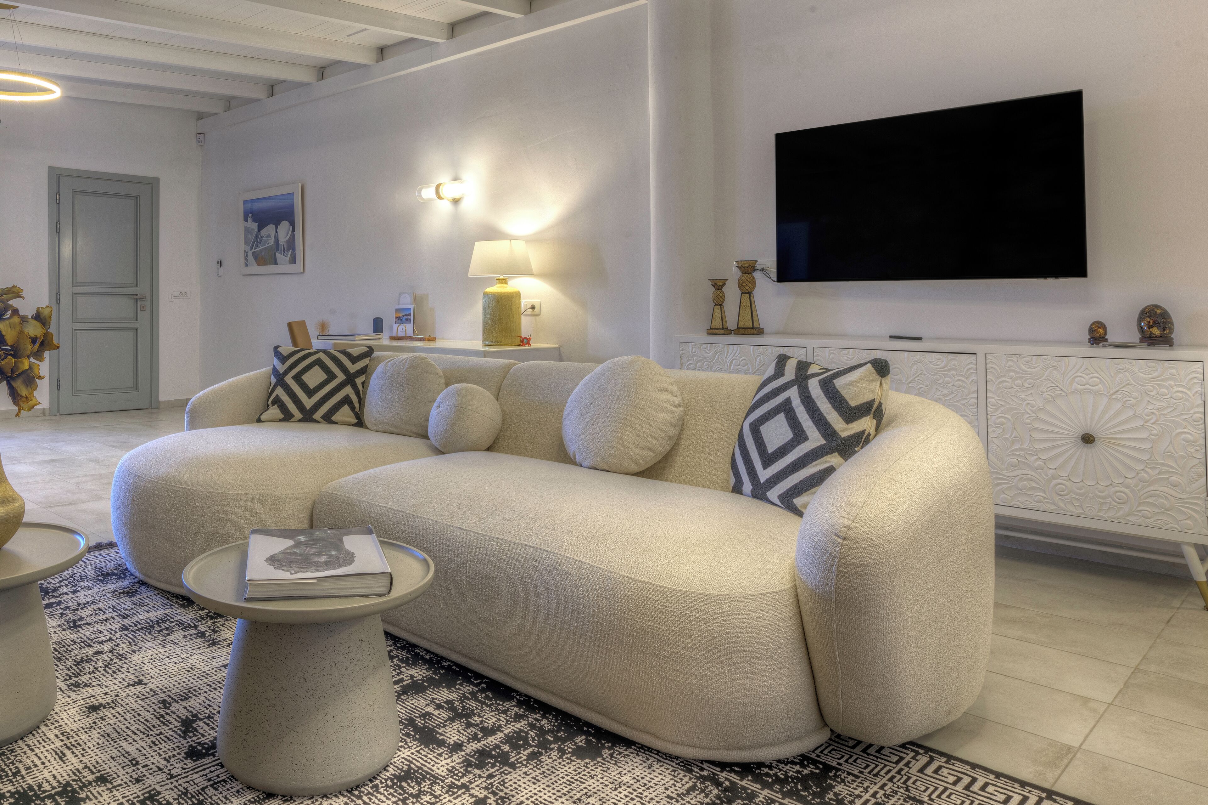 En moderne stue med en hjørnesofa, et sofabord, et fladskærms-tv og en dekorativ lampe.