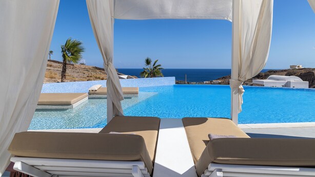 Vista a la piscina con dos sillas de descanso, cielo azul despejado y vista al mar.