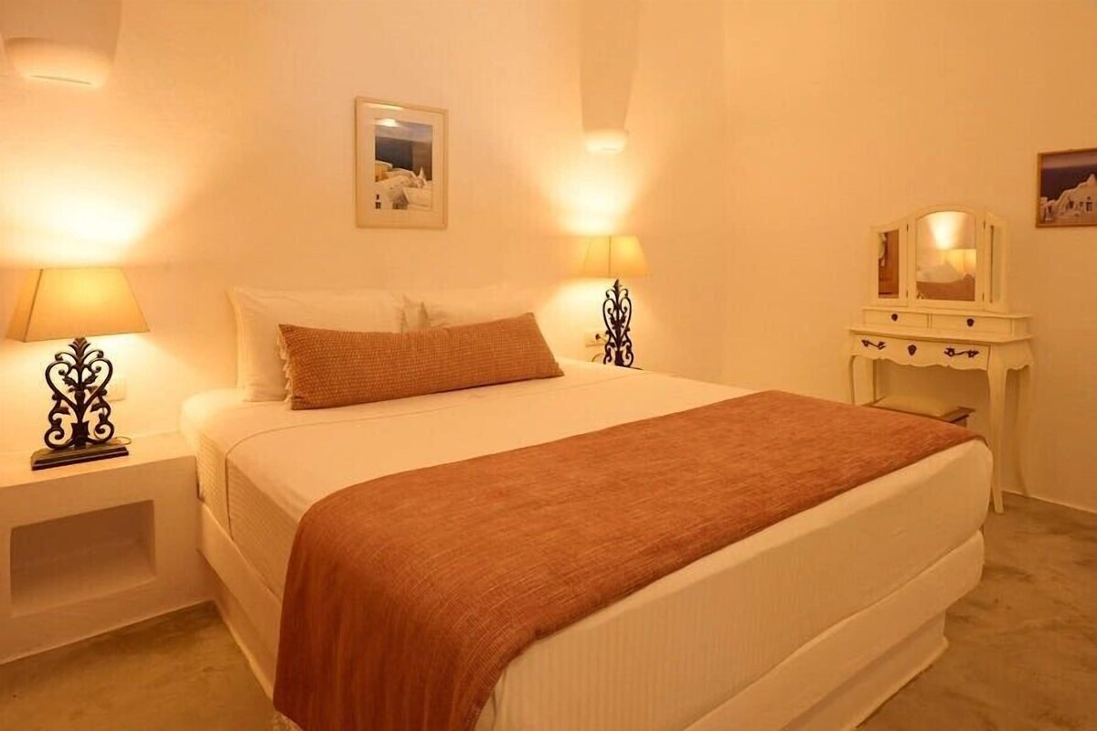 Une chambre d’hôtel avec un lit, deux tables de chevet avec des lampes, une commode et un tableau encadré au mur.