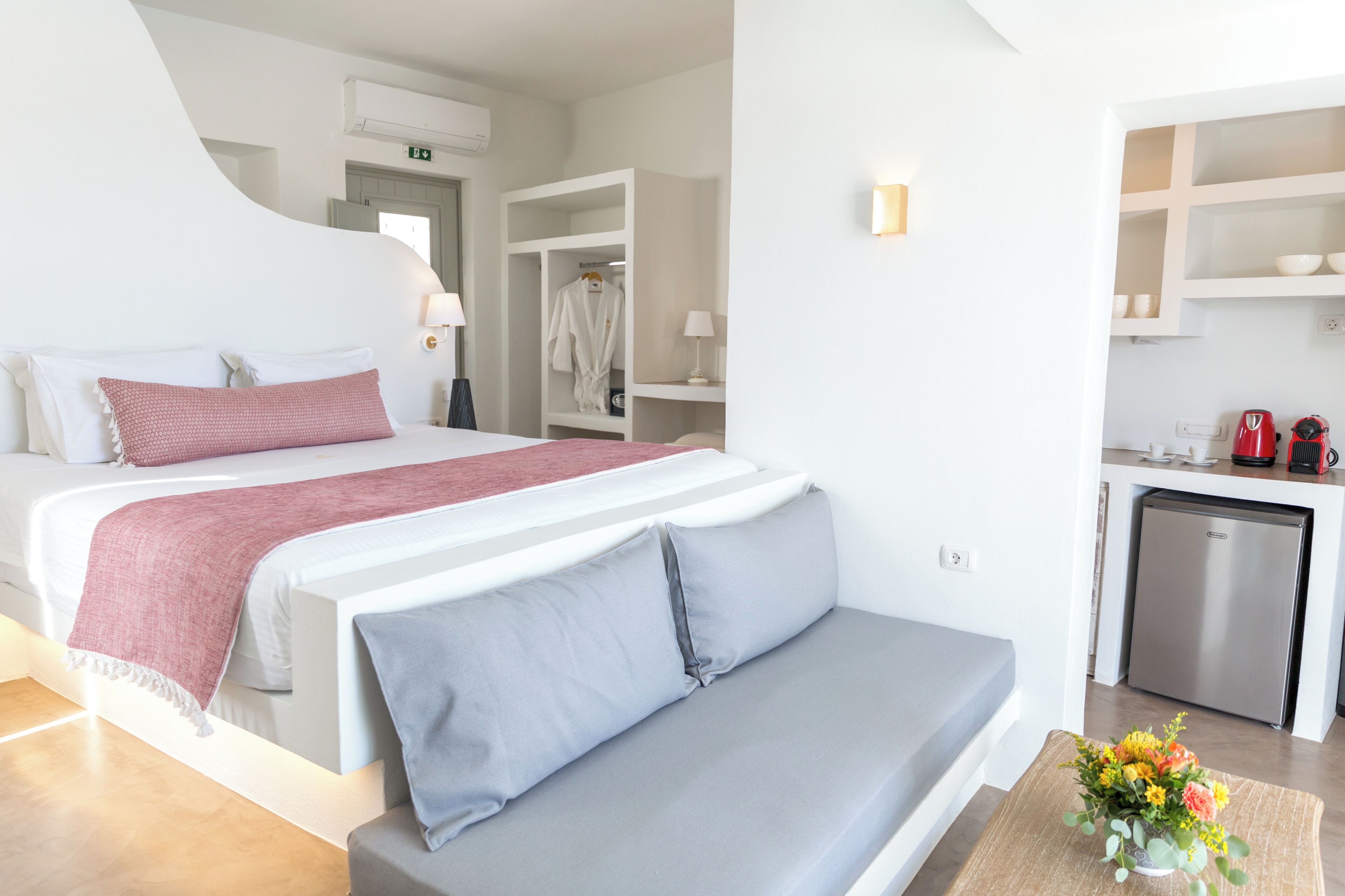 A modern hotel room with a large bed, a sofa, a kitchenette, and a walk-in closet.